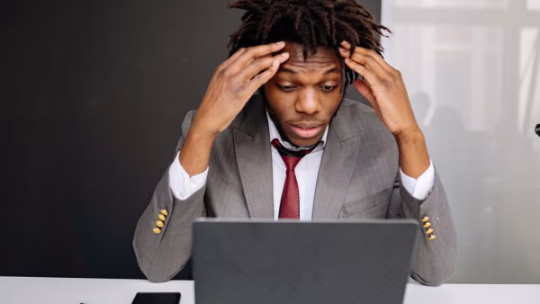 Gefrustreerde ondernemer met de handen tegen zijn hoofd achter een laptop op kantoor
