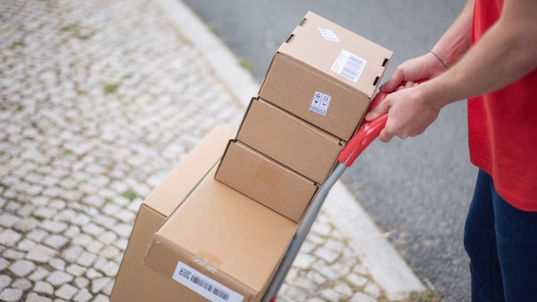 Bezorger duwt een karretje met pakketten over een geplaveide straat
