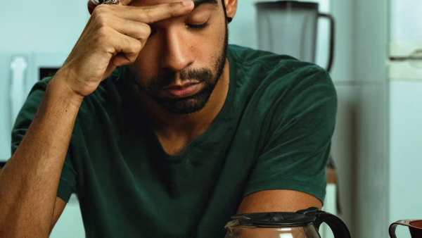 Man zit met de hand tegen zijn voorhoofd aan de keukentafel, gestrest over zijn financiën