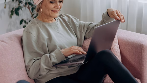 Oudere vrouw kijkt op de bank naar het scherm van haar laptop