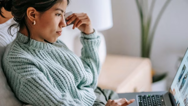 Vrouw rekent thuis af met een bankpas achter haar laptop