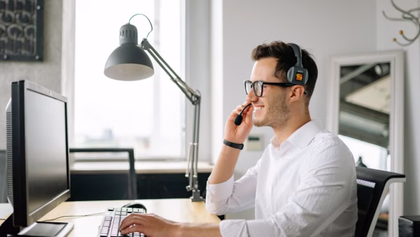Glimlachende medewerker met headset beantwoordt een klantvraag achter zijn computer