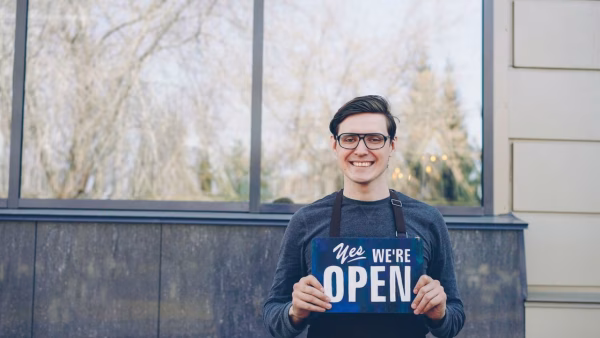 Lachende winkeleigenaar houdt een open bord vast voor zijn winkel