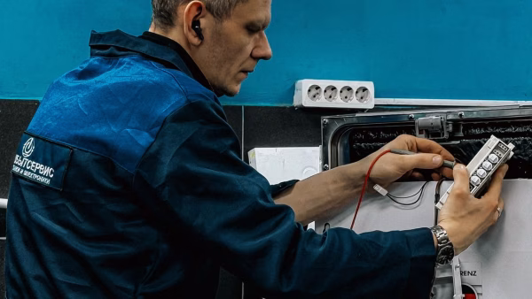 Technicus in blauwe werkkleding repareert een huishoudelijk apparaat