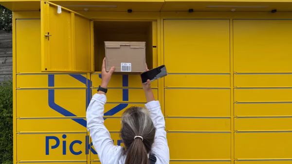 Vrouw legt een pakket met QR-code op haar telefoon in een gele pakketautomaat
