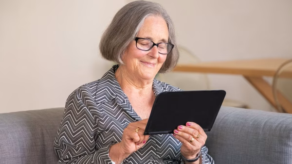 Oudere vrouw glimlacht terwijl ze een tablet gebruikt op de bank
