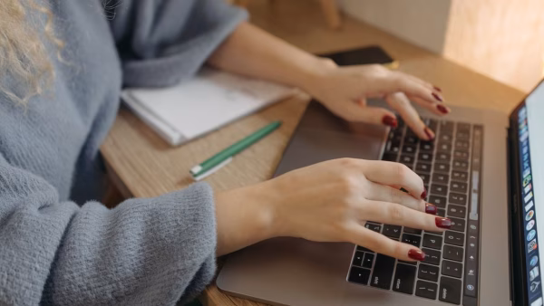 Close-up van handen die een productbeschrijving typen op een laptop aan een houten bureau