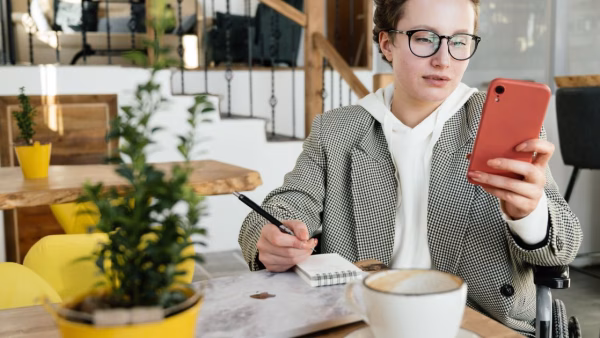 Vrouw in rolstoel bekijkt een webshop op haar smartphone in een café