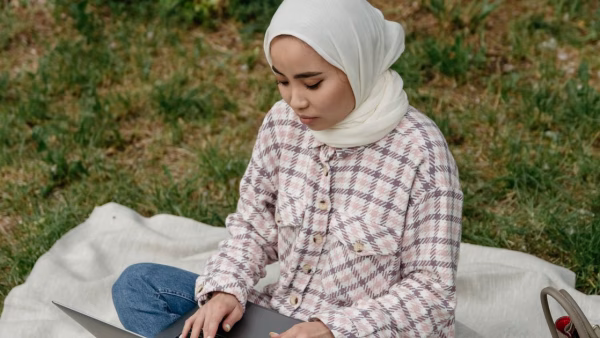 Jonge vrouw werkt buiten op een kleed in het park op haar laptop